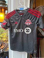 Front view of black and red Adidas Toronto FC kids jersey hanging on hanger