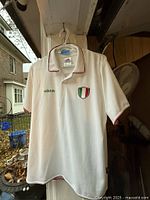 Front view of white Adidas Italia shirt hanging on hanger