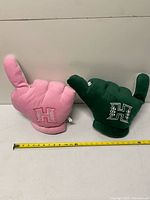 Pink and green University of Hawaii plush hand pillows side by side with ruler for scale