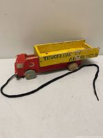 Side view of wooden pull toy truck showing red cab, yellow bed text and pull string
