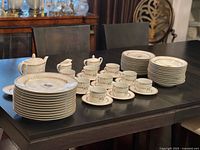 Full dinnerware set stacked on table showing plates, bowls, cups, teapot, sugar bowl, creamer
