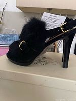 Side view of one shoe showing black suede, rabbit fur, buckle, stiletto heel on Coach box