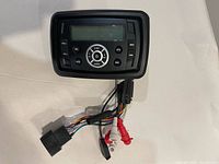 Front view of waterproof marine stereo head unit with display, control buttons and attached wiring harness