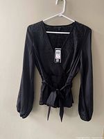 Front view of black Guess wrap blouse on hanger showing belt and long sleeves