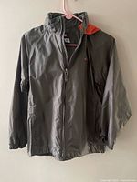 Front view of gray jacket on hanger showing full zipper and orange hood lining
