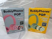 Front view of two boxed BuddyPhones POP Fun wireless headphones, pink and mint green versions