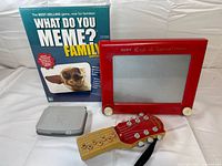 Group shot showing What Do You Meme? box, Etch A Sketch, grey Nintendo DS Lite, and AirGuitar toy