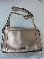 Front view of rose metallic crossbody bag showing chain strap, exterior slip pocket, logo plaque