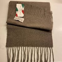 Folded taupe wool scarf showing fringe and attached tag