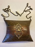 Full view of brass handbag showing shape, copper band, chain strap, ornate clasp