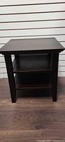 Front view of dark wood end table showing square top, two lower shelves, straight legs