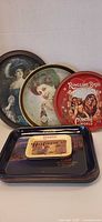 Group of vintage advertising metal trays; three round trays standing, small rectangular Carnation tray on top of stack of rectangular trays