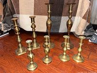 Group shot of all eight brass candlesticks on wood floor