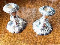 Pair of silver-plated ornate candlesticks on wood surface