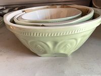 Stacked view of three pale green nesting bowls showing exterior color, white interiors, and rim chips