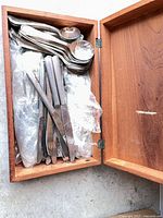 Open wooden box showing assorted silver-plated flatware wrapped in plastic