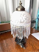 Full view of lamp showing glass shade, beaded fringe, metal base, and cord