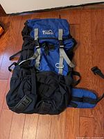 Front view of blue/black Trekk backpack showing top lid, front pockets, compression straps