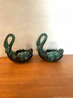 Pair of green drip glaze ceramic swan trinket holders on wood surface