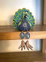 Front view of peacock shelf sitter showing body, tail and dangling gem legs