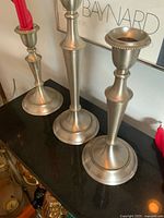Three silver-tone candlesticks displayed upright