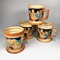 Four ceramic moustache steins grouped to show moulded tavern scene and handles.