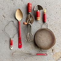 All six red wood-handled utensils laid out on concrete