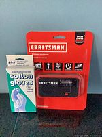 Craftsman weather radio in sealed packaging next to boxed cotton gloves