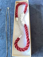 Red cord bracelet in box beside gold-tone chain
