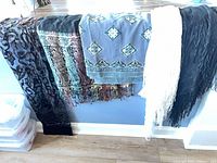 Overview of five scarves draped over railing showing colors, patterns, and fringe