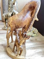 Carved wood grazing giraffe with calf; brass giraffes in background; clear acrylic giraffe; resin sitting giraffe; small block-mounted giraffe