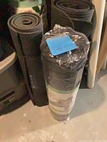 Three rolled fitness mats standing upright: two used black mats and one sealed new mat