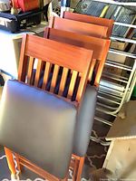 Stack of four folding wooden chairs showing brown finish and black padded seats