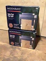 Front view of two boxed Moonrays solar post cap lights