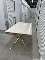 Table closed, glossy white top, gold X-legs visible