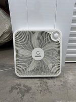 Front view of Genesis white 20-inch square box fan showing blades, grille, rotary dial control, and logo