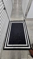 Black rug with white borders displayed on floor