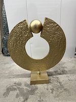 Gold textured circular sculpture with sphere and central cut-out