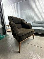 Front/side view of dark brown armchair showing upholstery, curved arms, seat cushion and wooden legs