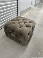 Taupe button-tufted cube ottoman shown on concrete floor