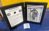 Two black wood frames side by side, left with description sheet, right with illustration, coin mounted