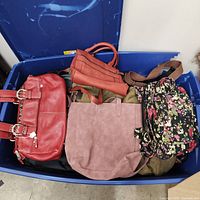 Top view showing red satchel, mauve tote, orange bag, olive bag and floral backpack purse in tote