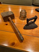 Wooden mallet, cast iron sad iron and clear glass insulator displayed on wooden surface