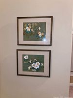 Both framed prints hung on wall showing floral and butterfly/bird imagery