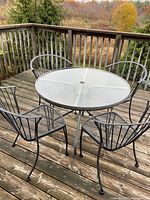 Round glass table and four black metal chairs on deck