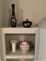 Shelf with all four items: tall black vase, black lidded bowl, white vase, floral ginger jar