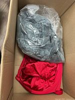 Grey garment in plastic and red satin garment visible in box