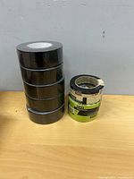 Five black duct tape rolls stacked beside three Scotch masking tape rolls