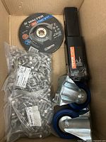 Overview of all items inside cardboard box: bolts, grinding wheel, casters, door closer