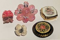 Group shot showing all five items: four brooches and one compact